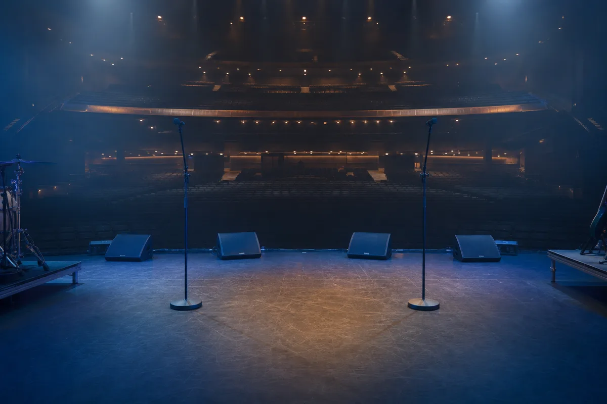 Plateau de petite salle de concert éclairé avant l&rsquo;arrivée des musiciens, câbles et pieds de micro en place