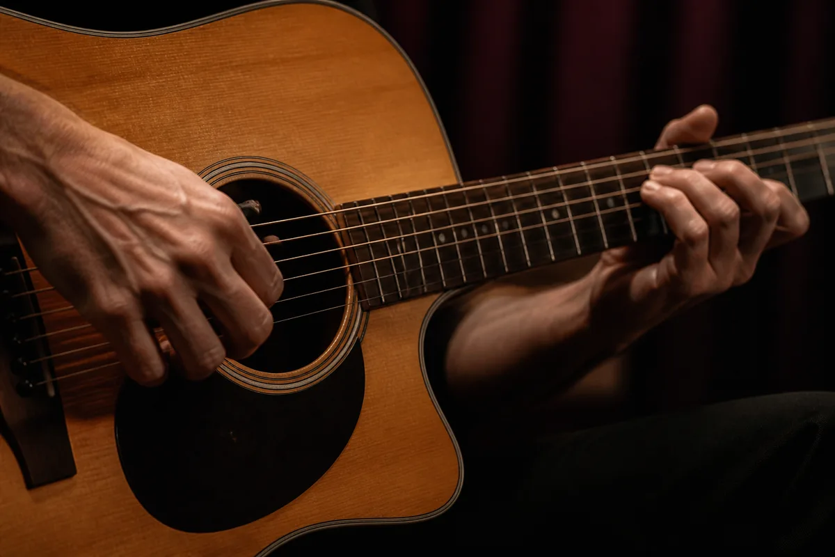 Mains de musicien posées sur une guitare avant l&rsquo;entrée en scène, lumière chaude de coulisses
